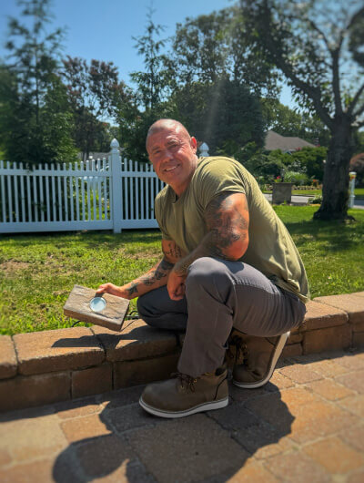Justin Brocking crouched on a paver wall, holding a low-voltage landscape light fixture